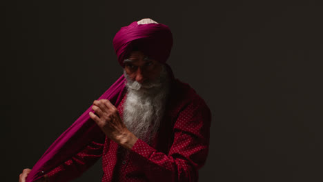 Toma-De-Estudio-Con-Iluminación-Tenue-De-Un-Hombre-Sikh-Mayor-Con-Barba-Atando-Una-Tela-Para-Hacer-Un-Turbante-Contra-Un-Fondo-Oscuro-3